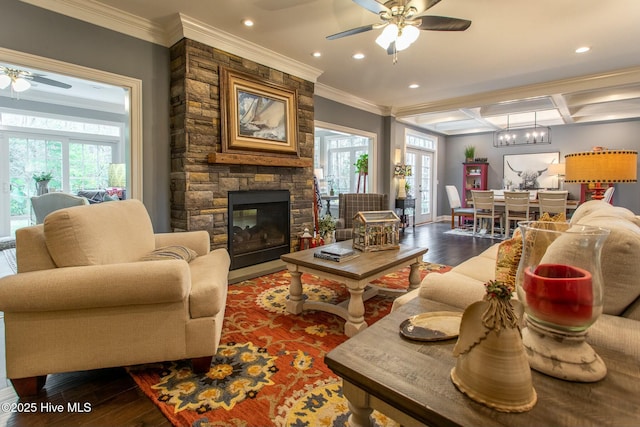 living room with a stone fireplace, coffered ceiling, wood finished floors, a ceiling fan, and crown molding