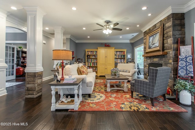 living room with ceiling fan, a stone fireplace, wood finished floors, ornamental molding, and ornate columns