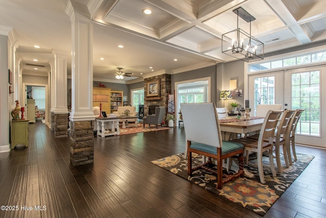 dining room with a stone fireplace, dark wood-style flooring, ornamental molding, beam ceiling, and decorative columns