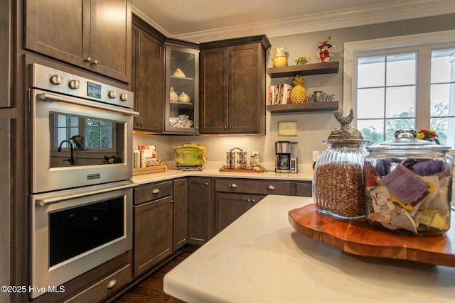 kitchen with ornamental molding, dark wood-style flooring, light countertops, dark brown cabinets, and stainless steel double oven