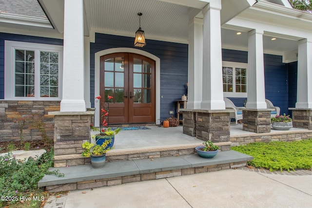 doorway to property with stone siding, a porch, and french doors