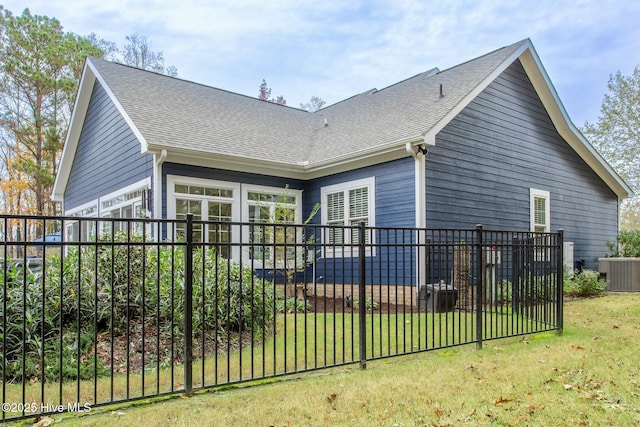 rear view of property with roof with shingles, a lawn, cooling unit, and fence