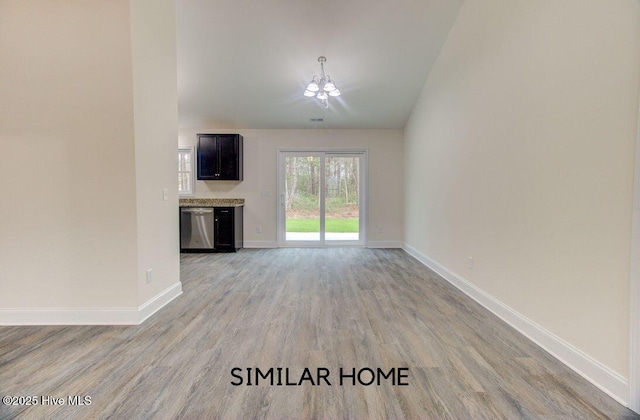 unfurnished living room with light wood-type flooring, vaulted ceiling, baseboards, and an inviting chandelier