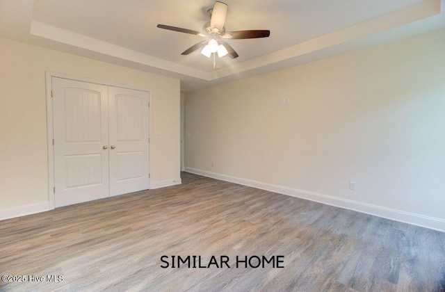 unfurnished bedroom featuring light wood finished floors, baseboards, a raised ceiling, ceiling fan, and a closet