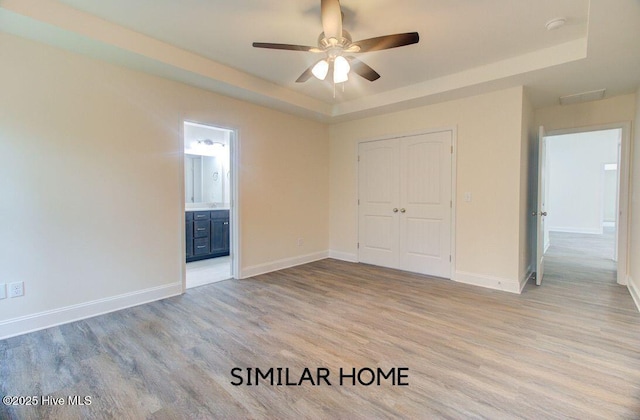 unfurnished bedroom with light wood finished floors, a raised ceiling, and baseboards