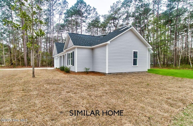 view of side of home featuring roof with shingles and a lawn