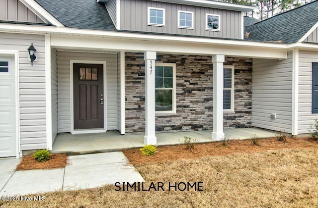 view of exterior entry featuring board and batten siding, covered porch, a shingled roof, and stone siding