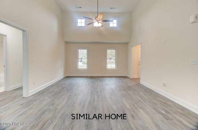 unfurnished living room with ceiling fan, plenty of natural light, wood finished floors, and baseboards