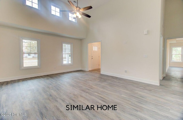 unfurnished room with a high ceiling, ceiling fan, baseboards, and wood finished floors