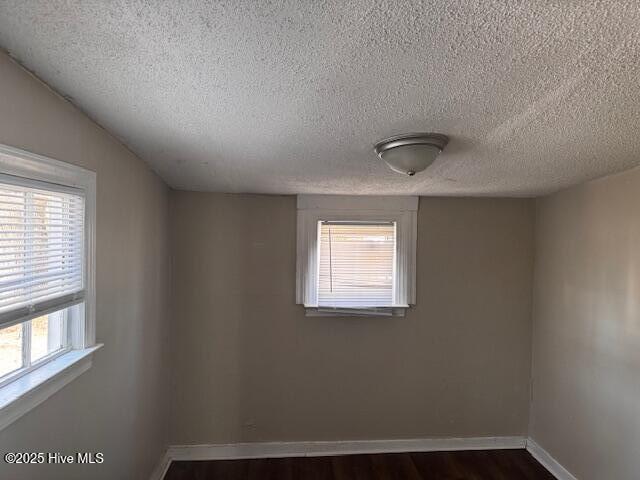 unfurnished room featuring a healthy amount of sunlight, dark wood finished floors, a textured ceiling, and baseboards