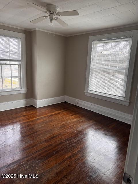 spare room featuring baseboards, ceiling fan, dark wood-type flooring, and crown molding