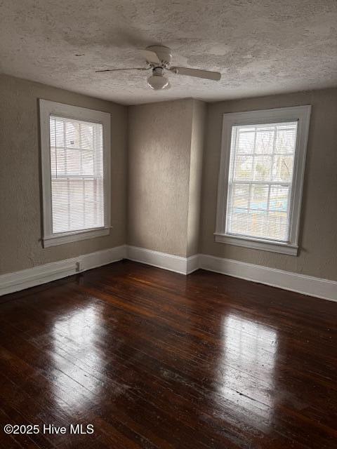 spare room featuring a wealth of natural light, dark wood-style flooring, and baseboards