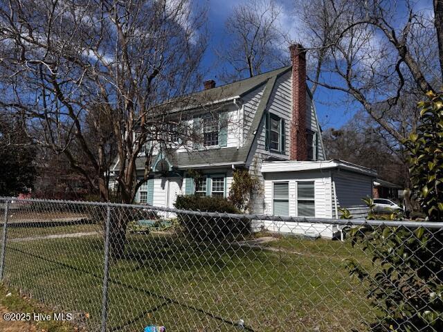 view of property exterior featuring a lawn, a chimney, fence, and a gambrel roof