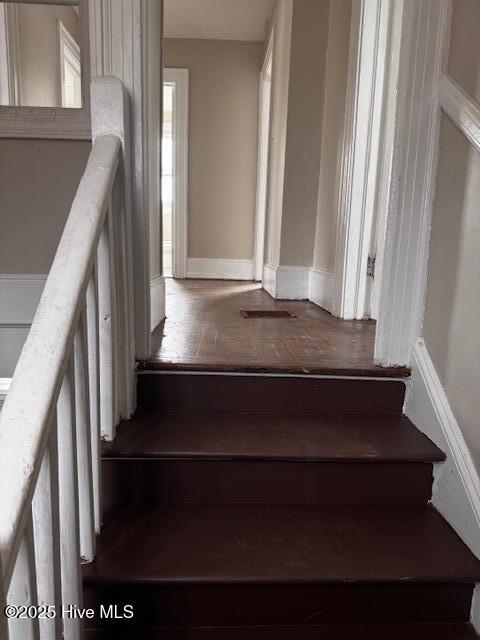 staircase with wood-type flooring, visible vents, and baseboards