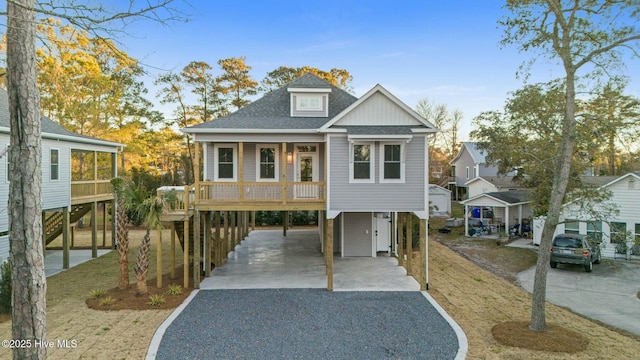 coastal inspired home featuring gravel driveway, a carport, covered porch, and roof with shingles