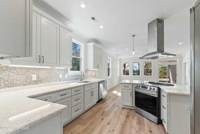 7103 E Yacht Dr, Oak Island, NC 28465 - kitchen featuring light wood finished floors, island exhaust hood, white cabinets, appliances with stainless steel finishes, and backsplash