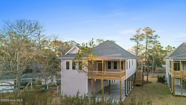 7103 E Yacht Dr, Oak Island, NC 28465 - rear view of property with driveway, a shingled roof, stairs, a carport, and a lawn