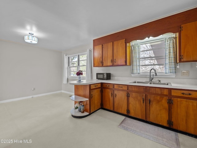 kitchen featuring brown cabinets, light countertops, a sink, and a peninsula