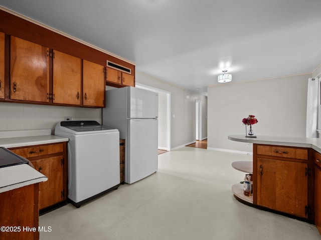 kitchen featuring brown cabinetry, freestanding refrigerator, washer / clothes dryer, and light countertops