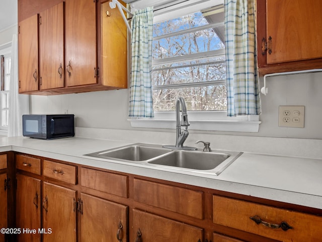 kitchen with black microwave, light countertops, a sink, and brown cabinets