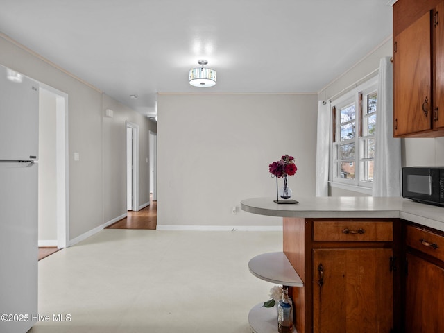 kitchen featuring brown cabinets, light countertops, freestanding refrigerator, black microwave, and a peninsula