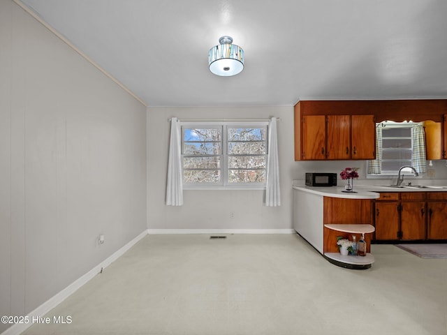 kitchen with light countertops, visible vents, brown cabinetry, a sink, and black microwave