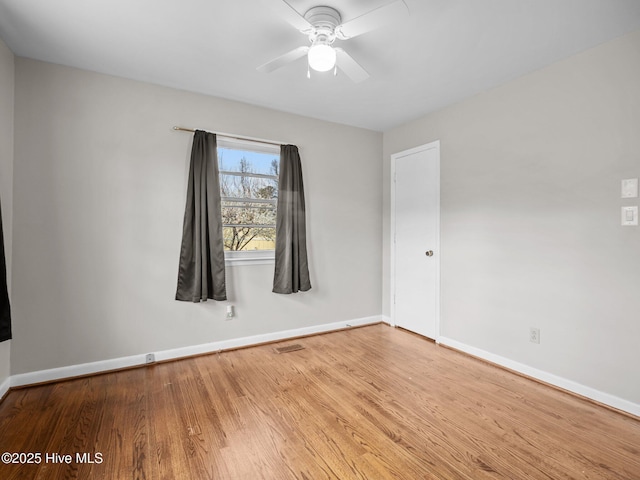 empty room with visible vents, wood finished floors, a ceiling fan, and baseboards