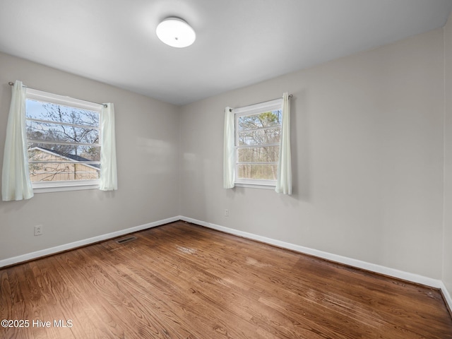 spare room with baseboards, visible vents, and wood finished floors