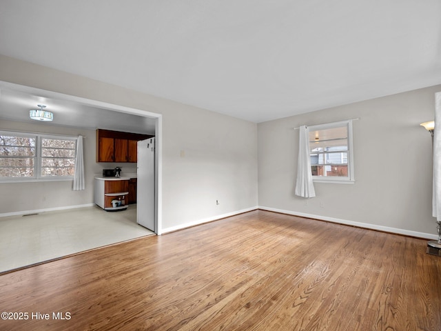 unfurnished living room with light wood-type flooring, baseboards, and a wealth of natural light