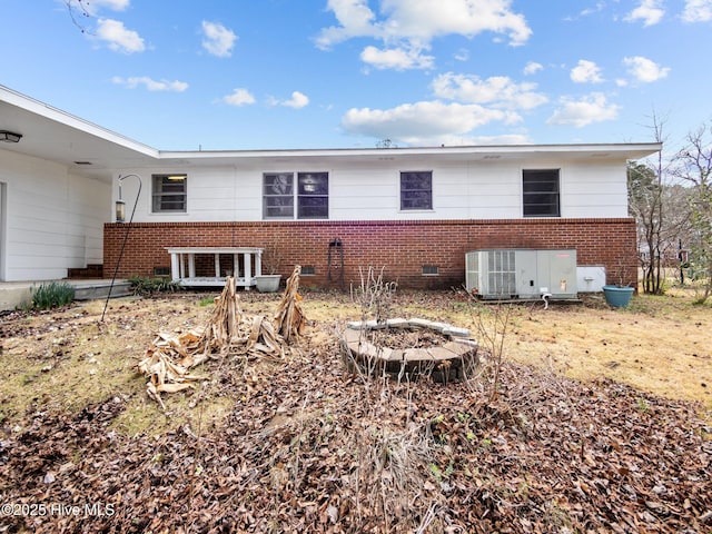 rear view of property with an outdoor fire pit, crawl space, brick siding, and central air condition unit