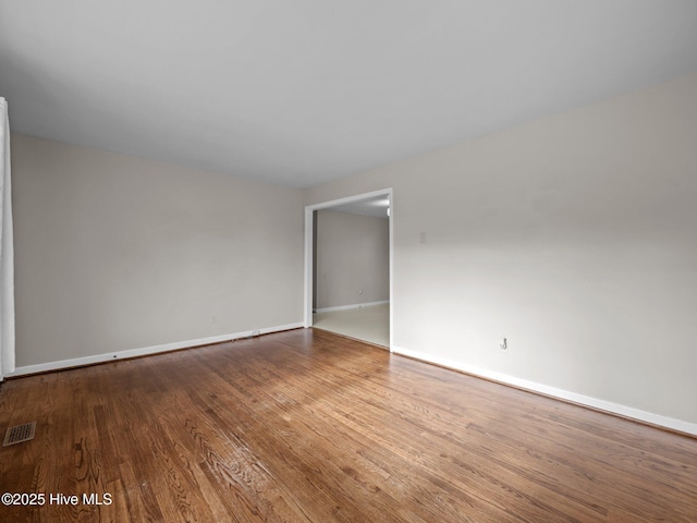 unfurnished room featuring visible vents, baseboards, and wood finished floors