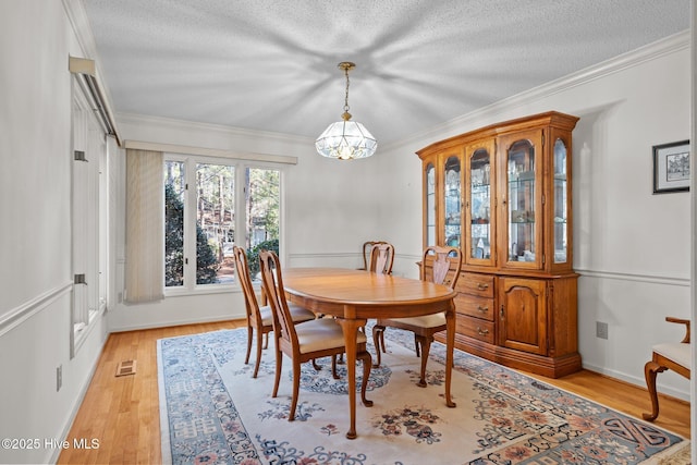 dining area featuring visible vents, crown molding, light wood-style floors, a notable chandelier, and a textured ceiling