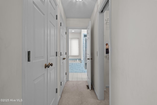 hallway featuring light tile patterned floors, light carpet, and a textured ceiling