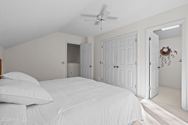 bedroom with ceiling fan, vaulted ceiling, a closet, a textured ceiling, and light colored carpet