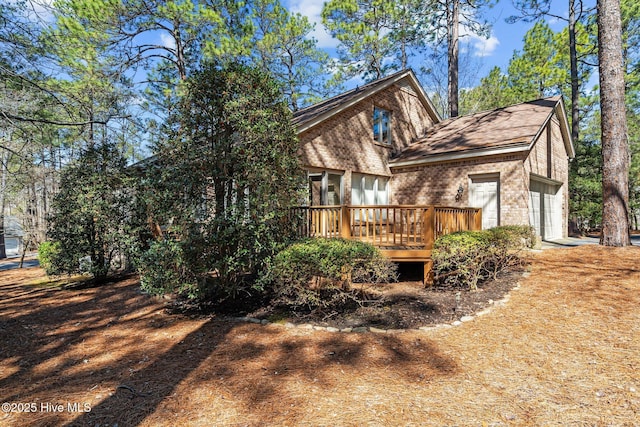 back of house with brick siding, a deck, and an attached garage