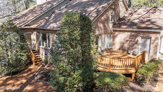 view of property exterior featuring a wooden deck, a chimney, brick siding, and a shingled roof