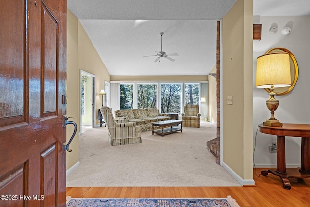 living area featuring a textured ceiling, wood finished floors, baseboards, ceiling fan, and vaulted ceiling