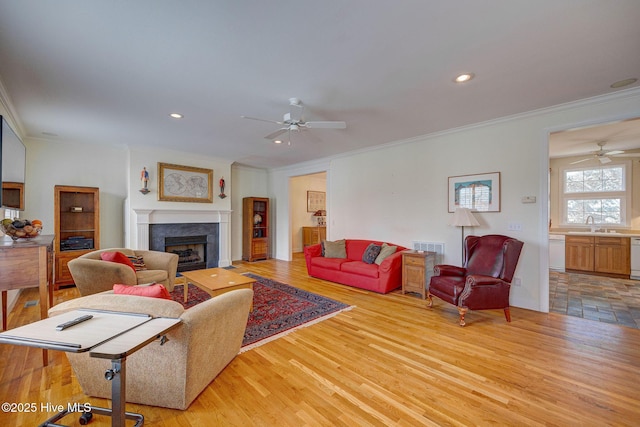 living area with crown molding, light wood-type flooring, a fireplace, and recessed lighting