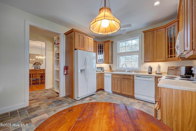 kitchen with white appliances, a sink, light countertops, stone finish floor, and glass insert cabinets