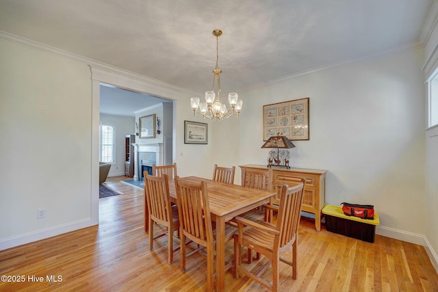 dining area with baseboards, light wood-style flooring, ornamental molding, an inviting chandelier, and a fireplace