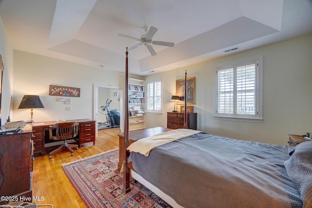 bedroom featuring a ceiling fan, a raised ceiling, visible vents, and light wood-style floors