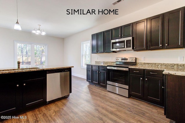 kitchen featuring visible vents, appliances with stainless steel finishes, wood finished floors, light stone countertops, and a sink