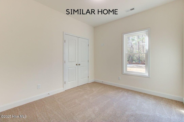 unfurnished bedroom featuring a closet, light colored carpet, visible vents, and baseboards