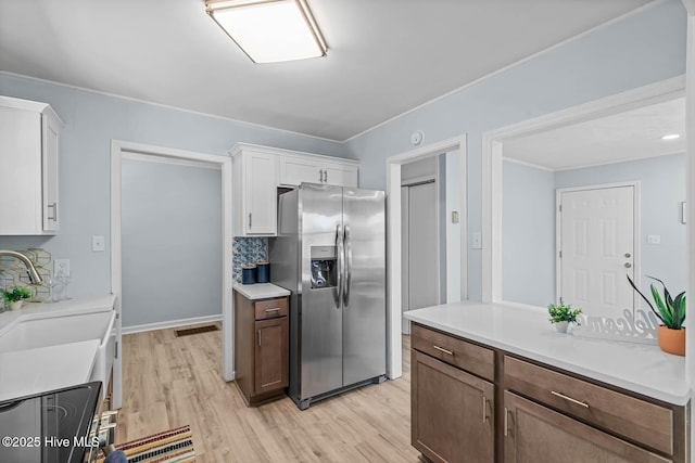 kitchen with light wood finished floors, stainless steel fridge, white cabinetry, and a sink