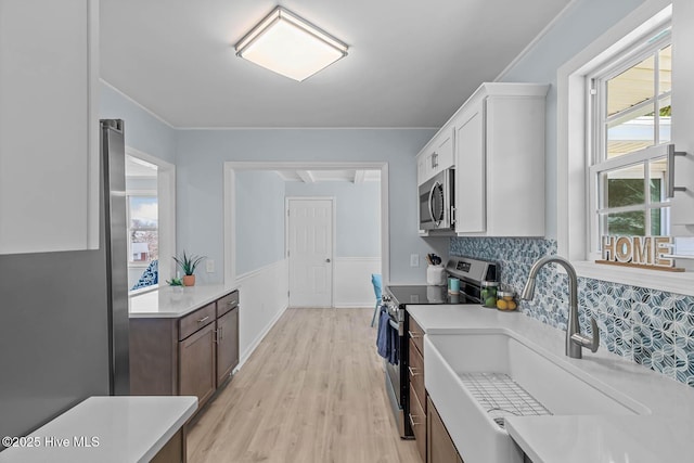 kitchen with plenty of natural light, a sink, light countertops, appliances with stainless steel finishes, and wainscoting