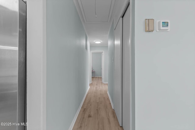 hall with light wood-style flooring, attic access, and baseboards