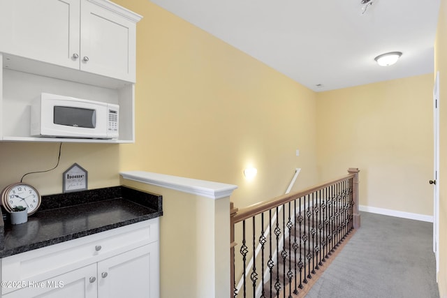 hallway featuring an upstairs landing, baseboards, and carpet floors