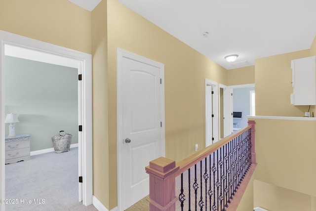 hall with an upstairs landing, carpet flooring, and baseboards