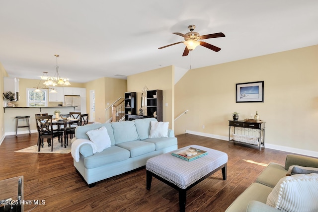 living area featuring stairway, baseboards, dark wood-style flooring, and ceiling fan with notable chandelier