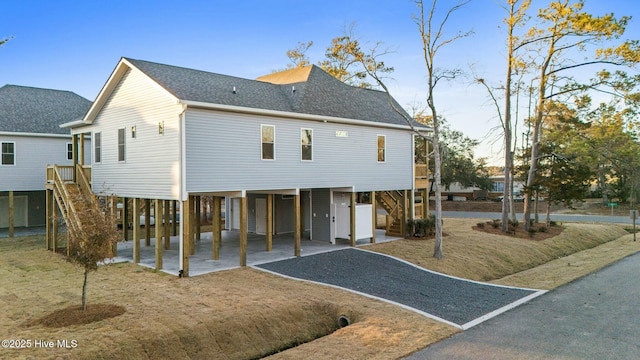 rear view of property featuring gravel driveway, stairs, roof with shingles, a carport, and a patio